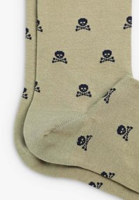 Calzini verde oliva con motivo di teschio e ossa incrociate navy. Realizzati in tessuto morbido, presentano polsini a coste e una superficie liscia.