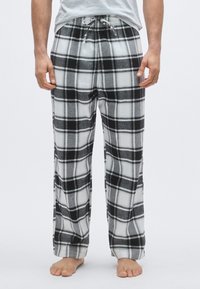 Rutet pysjamasbukse i svart, hvitt og grått flanell. Har elastisk midjebånd med snor, rett ben og myk tekstur.