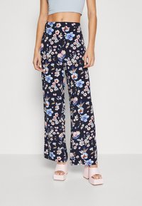 Woman wearing high-waisted, wide-leg pants with blue and pink floral print, paired with light pink platform sandals.