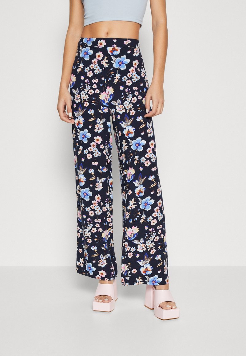 Woman wearing high-waisted, wide-leg pants with blue and pink floral print, paired with light pink platform sandals.