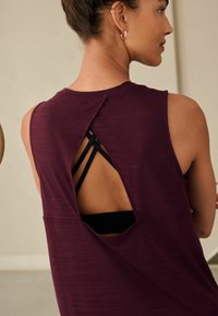 Top fără mâneci, de culoare burgundy, cu o decupare în spate ce dezvăluie bretele negre, dintr-un material texturat și cu o croială lejeră. Dispune de un guler rotund.