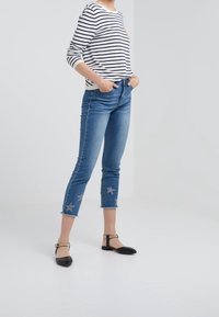 Chemise à manches longues rayée blanche et marine avec une poche poitrine, associée à un jean bleu court orné d'étoiles et à ourlets effilochés.