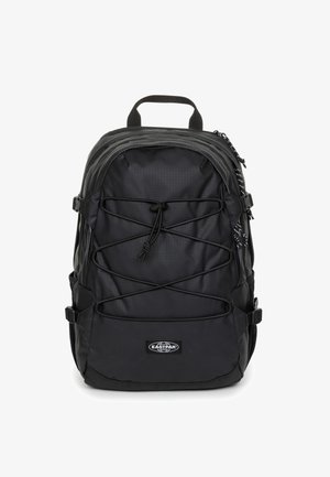 Mochila negra con un diseño elegante de nailon, parte superior curva, cordón frontal elástico ajustable, bolsillos laterales y logotipo de Eastpak en la parte inferior.
