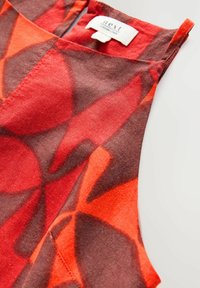 Ärmelloses Top mit rot-braunem Muster und einem Etikett, das eine glatte Textur und ein mutiges, abstraktes Design aus überlappenden Formen aufweist.