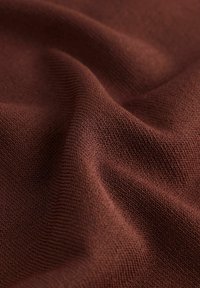 Tissu tricoté marron, présentant une texture lisse avec un motif subtil de fines nervures et de doux plis, mettant en valeur la profondeur et la dimension.