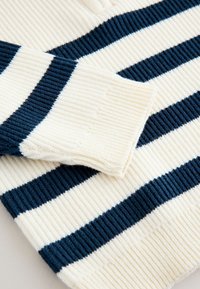 Maglione a maglia a coste con strisce orizzontali alternate blu navy e crema; presenta maniche con polsini e una texture morbida.