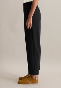 Pantalons noirs amples avec une taille élastique, assortis à des baskets en daim marron avec des accents roses et des lacets texturés.