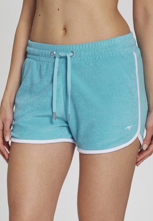 Woman wearing light blue terry cloth shorts with white trim and drawstring, showing midriff and hands resting at sides.