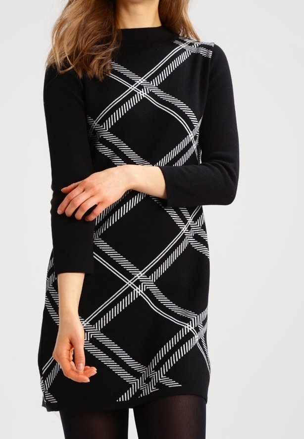 Czarna sukienka z białym, ukośnym paskowanym wzorem, długimi rękawami, wysokim dekoltem i lekko rozkloszowanym dołem, wykonana z miękkiego materiału.