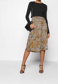 Černý top s dlouhým rukávem v kombinaci s sukní ke kolenům se vzorem leopardího potisku v hnědé a černé barvě. Doplněno malou černou kabelkou a podpatky.