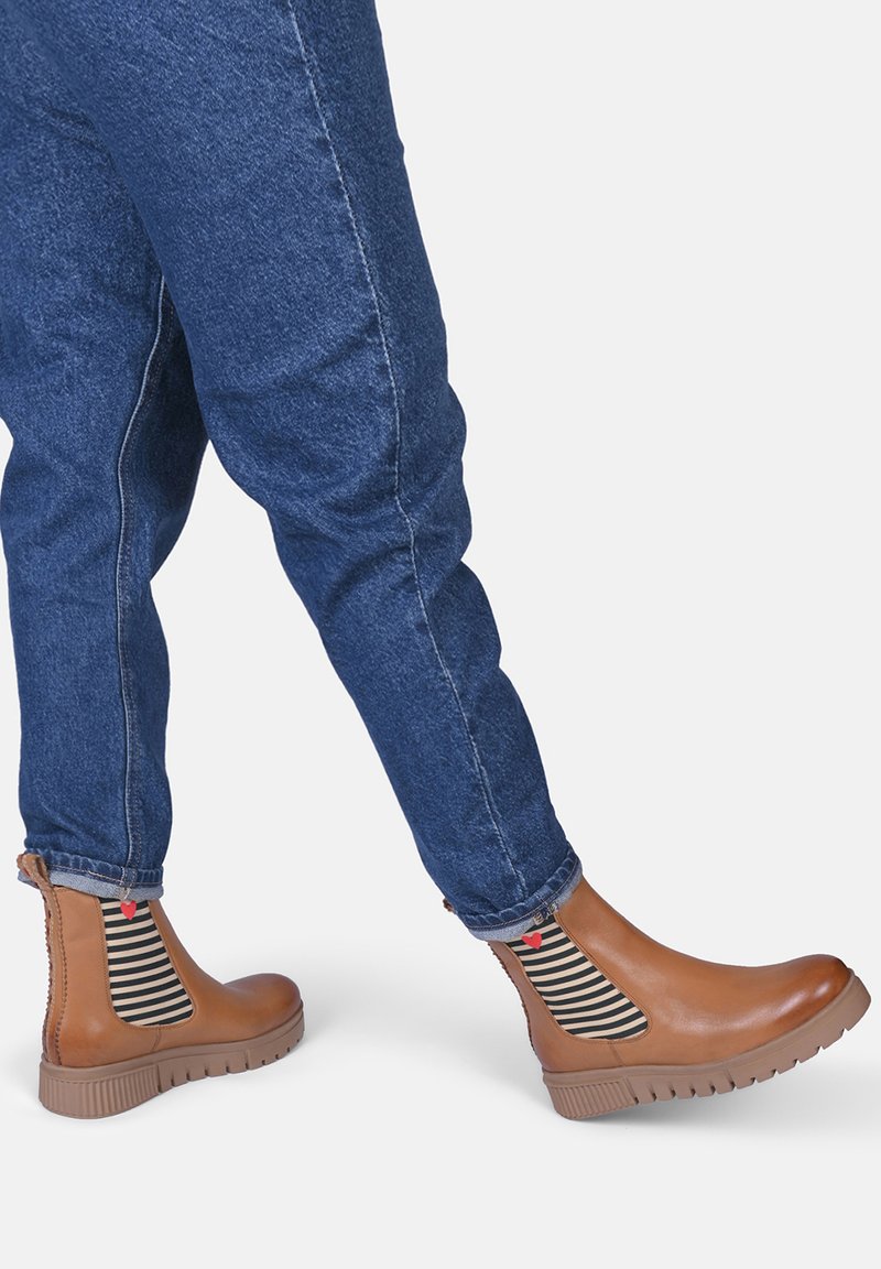 Bottes chelsea marron avec une finition lisse, panneaux latéraux élastiques rayés et semelles en caoutchouc texturées, portées avec un jean en denim bleu.