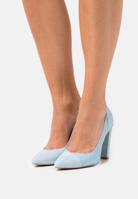 Ljusblå högklackade skor med spetsig tå, med en slät lädertextur och en kontrasterande matt tåhuvuddesign.