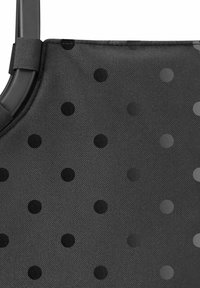 Bolsa de tela negra con una superficie texturizada, que presenta lunares de diferentes tamaños en negro sólido y gris sobre un fondo oscuro.