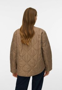 Quiltad beige jacka med en lös passform, som har en slät yta och rundad fåll. Baksidan visar ett diamantmönster i tyget.