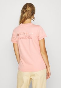 Rosa bomulls t-shirt med korta ärmar. Har texten "adidas" och "sport" i en ljusare nyans på baksidan. Rund halsdesign.