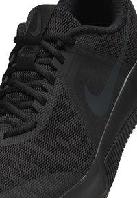 Schwarzer Sportschuh mit einem Obermaterial aus Netzgewebe, strukturierten Oberflächen und einer Gummisohle. Enthält ein auffälliges Nike-Logo an der Seite.