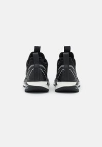 Mustat urheilukengät, joissa on teksturoitu päällinen harmailla yksityiskohdilla, pehmustettu nilkkareuna ja valkoinen välipohja. Takana olevat vetotikut parantavat käyttömukavuutta.