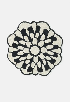 Tapis rond noir et blanc avec des bords ondulés et un motif floral qui rayonne du centre en formes alternées noires et blanches.