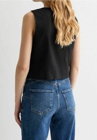 Svart ärmlös crop top som kombineras med högmidjade blå denimjeans med en klassisk femficksdesign och en urtvättad textur.