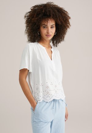 Blusa blanca de manga corta con escote en V y dobladillo bordado que presenta detalles florales y de ojal. Combinada con pantalones de rayas azul claro.