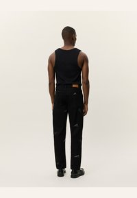 Top negro sin mangas combinado con jeans negros que presentan sutiles patrones triangulares. Los jeans tienen una etiqueta de cuero marrón en la parte posterior.