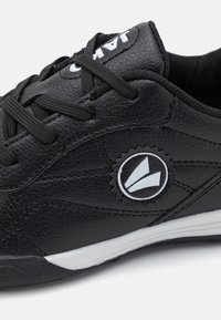 Sorte lædersneakers med en tekstureret overflade, der har sorte snørebånd, et cirkulært logo i hvid, og en kontrasterende hvid sål.