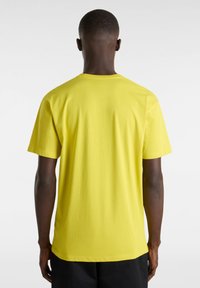 Camiseta de algodón amarilla con mangas cortas, cuello redondo y una textura suave, vista por detrás. Destacan su diseño minimalista.