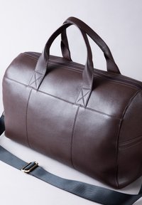 Brown leather duffel bag with dual top handles, zipper closure, textured surface, and adjustable black fabric shoulder strap.