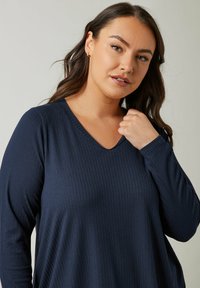 Maglietta a maniche lunghe blu navy con scollatura a V e texture a coste, caratterizzata da una vestibilità comoda e maniche leggermente oversize, realizzata in un tessuto morbido.