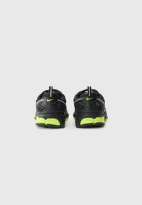 Baskets de sport noires avec une tige en maille texturée, accents vert fluo et boucles de tirage au talon. Présente une semelle extérieure rembourrée pour plus de confort.