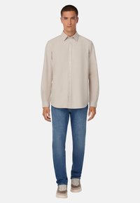 Camisa de botón de manga larga color beige claro con cuello extendido, combinada con jeans azules y zapatillas beige. Textura suave, ajuste a medida.