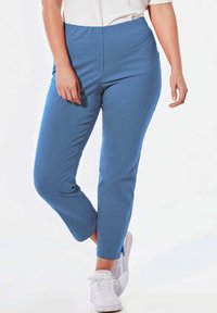 Blauwe stretchbroek met een gladde textuur, taps toelopende pijpen en een elastische tailleband, gecombineerd met witte sneakers.