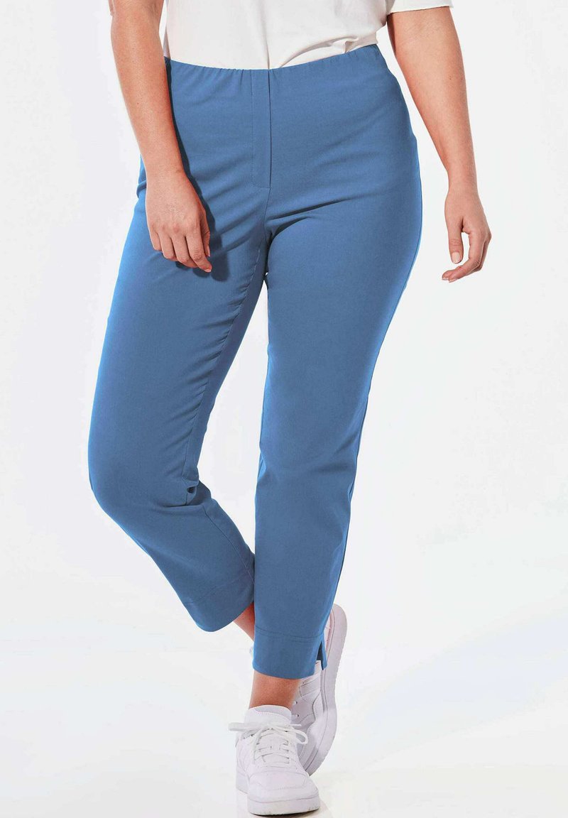 Blauwe stretchbroek met een gladde textuur, taps toelopende pijpen en een elastische tailleband, gecombineerd met witte sneakers.