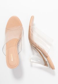 Peep-toe klackar med en nude matt sula och genomskinlig PVC-rem, med en transparent kilklack och diskret varumärke på insidan.