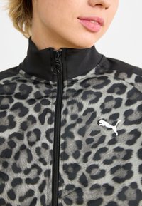 Giacca con zip in fantasia leopardata, caratterizzata da un alto colletto, accenti neri e un logo bianco. Realizzata in tessuto liscio e leggero con texture.