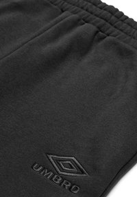 Los joggers negros de tejido suave cuentan con una cinturilla elástica y un discreto logotipo bordado de Umbro. Textura lisa sin patrones distintivos.