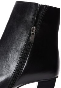 Bottine en cuir noir avec fermeture éclair latérale et talon bloc, finition lisse et couture visible le long de la couture de la fermeture éclair.