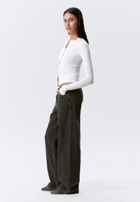 Chemise blanche à manches longues et boutonnière associée à un jean ample gris foncé. L'ensemble se compose d'un haut ajusté et d'un pantalon décontracté et volumineux.