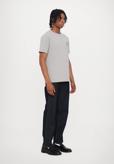 Gray cotton t-shirt with a rounded neckline and short sleeves. Paired with dark blue denim pants, worn with black shoes.