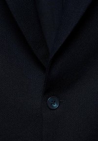 Mornarski sako s detaljima od teksturirane tkanine, s izrezanim reverima i okruglim crnim dugmetom sa četiri rupe.