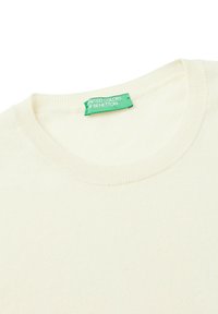 Maglione a girocollo color crema con un'etichetta verde "United Colors of Benetton" cucita all'interno del colletto.