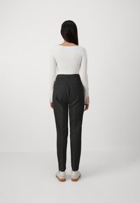 Svarta skräddarsydda byxor med hög midja, två bakfickor och en slim fit, i kombination med en figurnära vit långärmad topp.