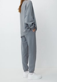 Szary dres z miękkiego materiału. Luźny krój z ściągaczami na rękawach oraz boczną kieszenią. Połączony z białymi trampkami.