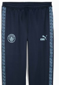 Marinefarbene Sporthosen mit einem strukturierten Taillenbund, versehen mit einem hellblauen Manchester City-Logo und Puma-Branding sowie gemusterten Seitenstreifen.