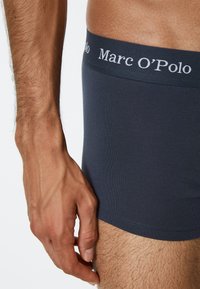 Mørk grå boxershorts laget av stretchstoff, med en myk elastisk midjebånd med "Marc O'Polo"-logo i hvitt. Glatt tekstur.
