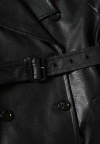 Černý kožený trench coat s páskem v pase, velkými knoflíky a detailním prošíváním. Povrch je hladký s jemným leskem.