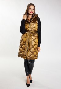 Vesta puffer aurie, cu umplutură matlasată, glug�ă, închidere cu fermoar și o curea asortată. Purtați-o peste un pulover negru și pantaloni negri strâmți. Tocuri ascuțite.