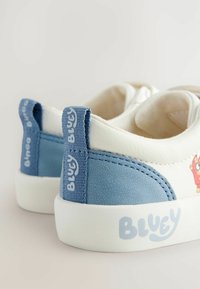 Witte en lichtblauwe sneakers met een gestructureerde afwerking, rubberen zolen en het "BLUEY" logo op de zijkant, met een cartoonfiguurdetail.