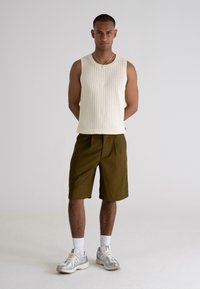 Cream ribbed sleeveless top paired with olive green shorts. Model wears white socks and gray athletic shoes with silver accents.