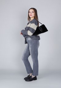 Maglione a strisce grigio e crema, jeans grigi, borsa nera con superficie texturizzata e scarpe nere. Sfondo di un grigio neutro.